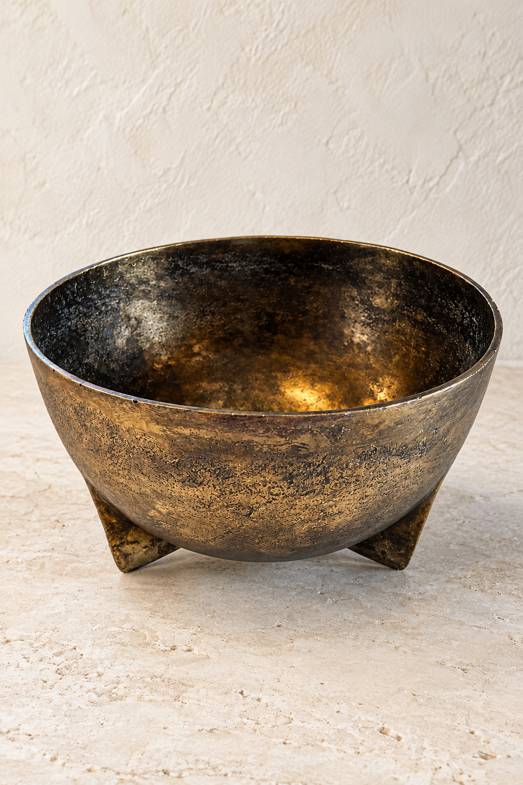 Poseidon antique gold metal bowl on three fin-shaped feet, showing its wide opening and mottled finish against a pale background.