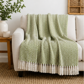 Green herringbone blanket with white tassels displayed over a sofa