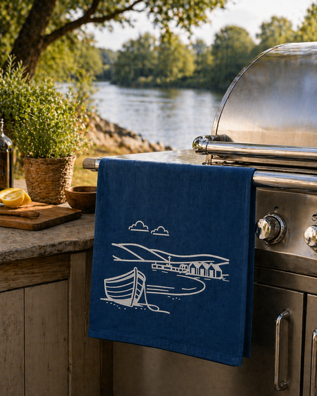 Blue towel with white boat design hanging on a grill outdoors by a river