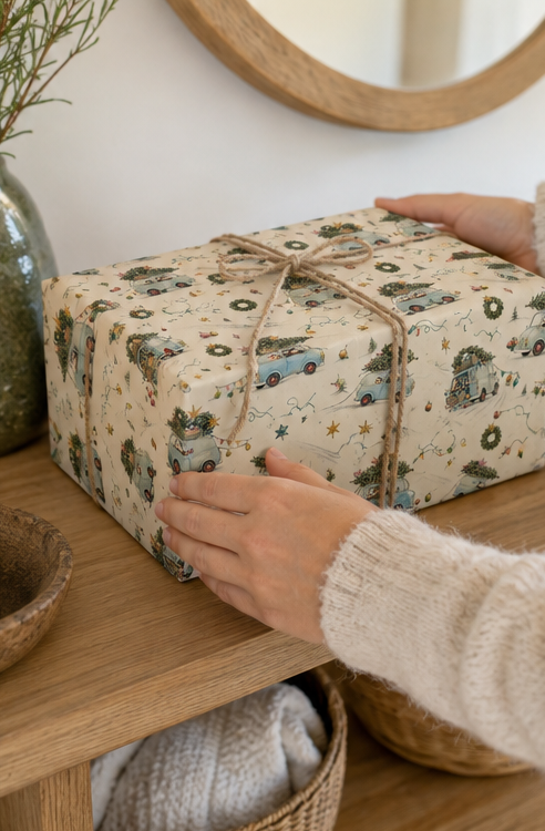 A badger is driving home for Christmas with a pale-blue vintage car piled high with trees, wreaths, crates and baubles. This pencil-sketch Christmas wrapping paper has muted festive colour on a warm ivory background and comes in two paper weights and three useful sizes.