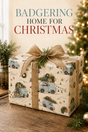 A Christmas-themed gift box wrapped in cream-colored paper with a vintage camper pattern, tied with a burlap ribbon and bow, sitting on a wooden table with festive background elements and the text 'BADGERING HOME FOR CHRISTMAS' at the top.