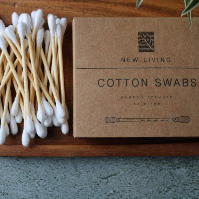 Bamboo Cotton swabs on a wooden tray with a cardboard box labeled 'New Living Cotton Swabs'.