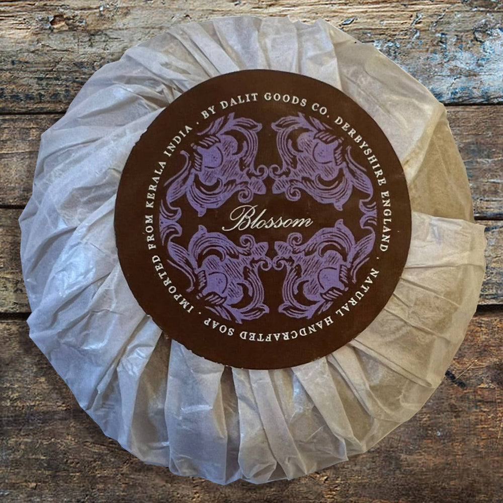 Bar of soap in a white paper wrap with a decorative label on a wooden surface