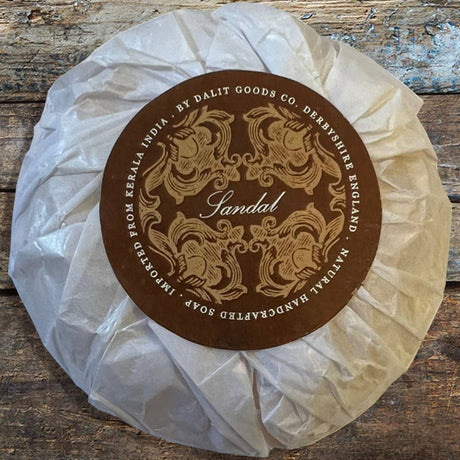 Bar of soap wrapped in white paper with a decorative brown label on a wooden surface
