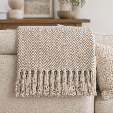 a beige herringbone patterned throw blanket with tassels on a sofa.