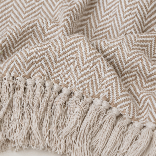 a beige herringbone patterned throw blanket with tassels
