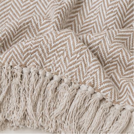 a beige herringbone patterned throw blanket with tassels