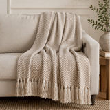 a beige herringbone patterned throw blanket with tassels on a sofa.