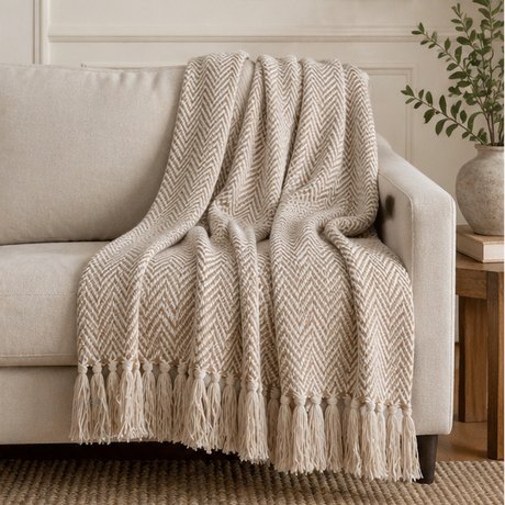 a beige herringbone patterned throw blanket with tassels on a sofa.
