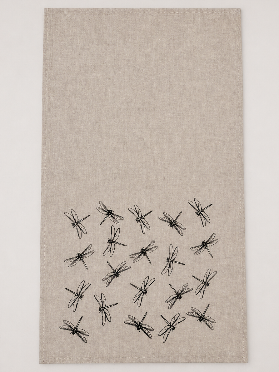 Beige tea towel with black hand printed dragonfly pattern on a white background