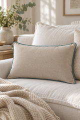 A linen cushion with duck egg piping, styled on a light beige sofa with a textured throw blanket and a neutral vase of flowers in the background.