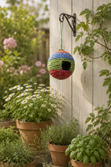 Colorful birdhouse hanging on a wooden wall with plants and flowers in the background