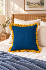 Blue 55 × 55cm linen cushion with mustard ruffle on ivory bedding with a slate-blue throw.