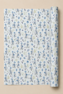 A roll of wrapping paper with a repeating pattern of Little Girls in blue dresses on a Powder Blue background, shown against a solid beige backdrop.
