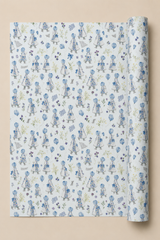 A roll of wrapping paper with a repeating pattern of Little Girls in blue dresses on a Powder Blue background, shown against a solid beige backdrop.