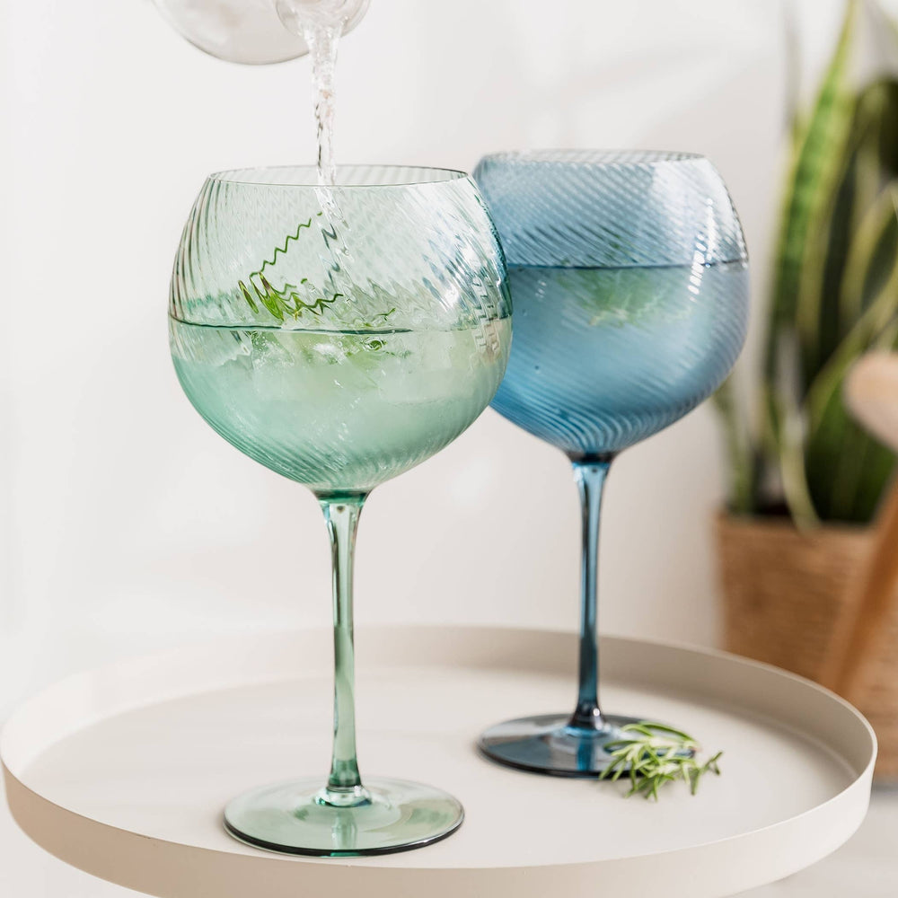 Two colorful gin glasses on a white surface with a blurred background