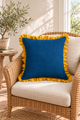 Square blue linen cushion with gathered mustard edging on a natural wicker armchair.