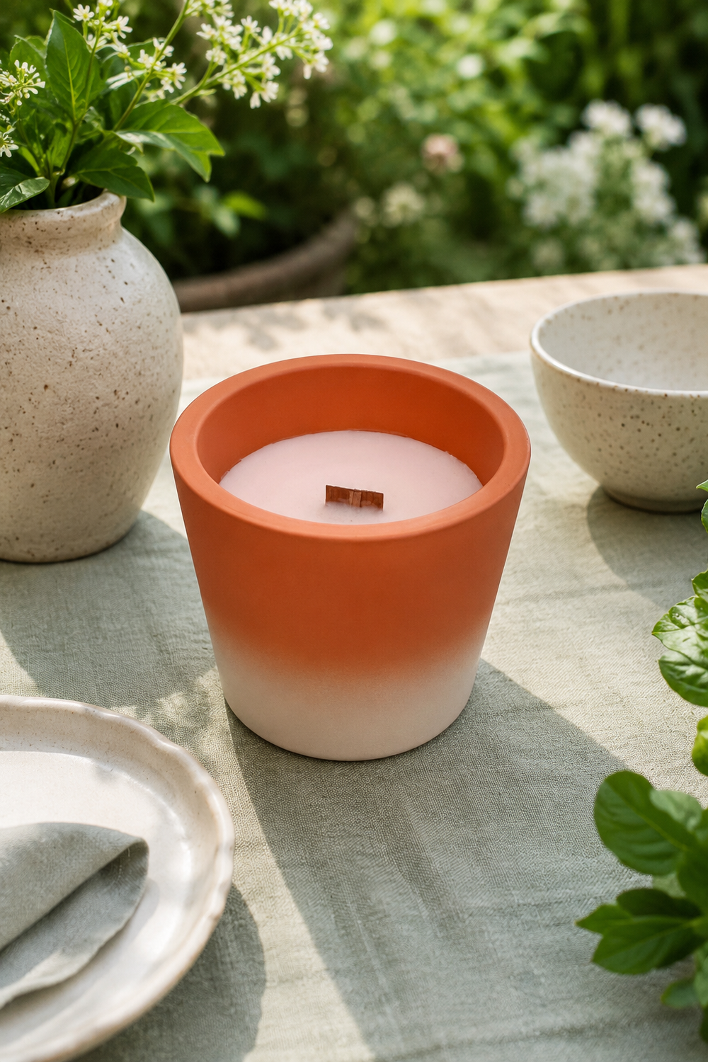 Candle in an orange and white terracotta pot on a table with plants in the background