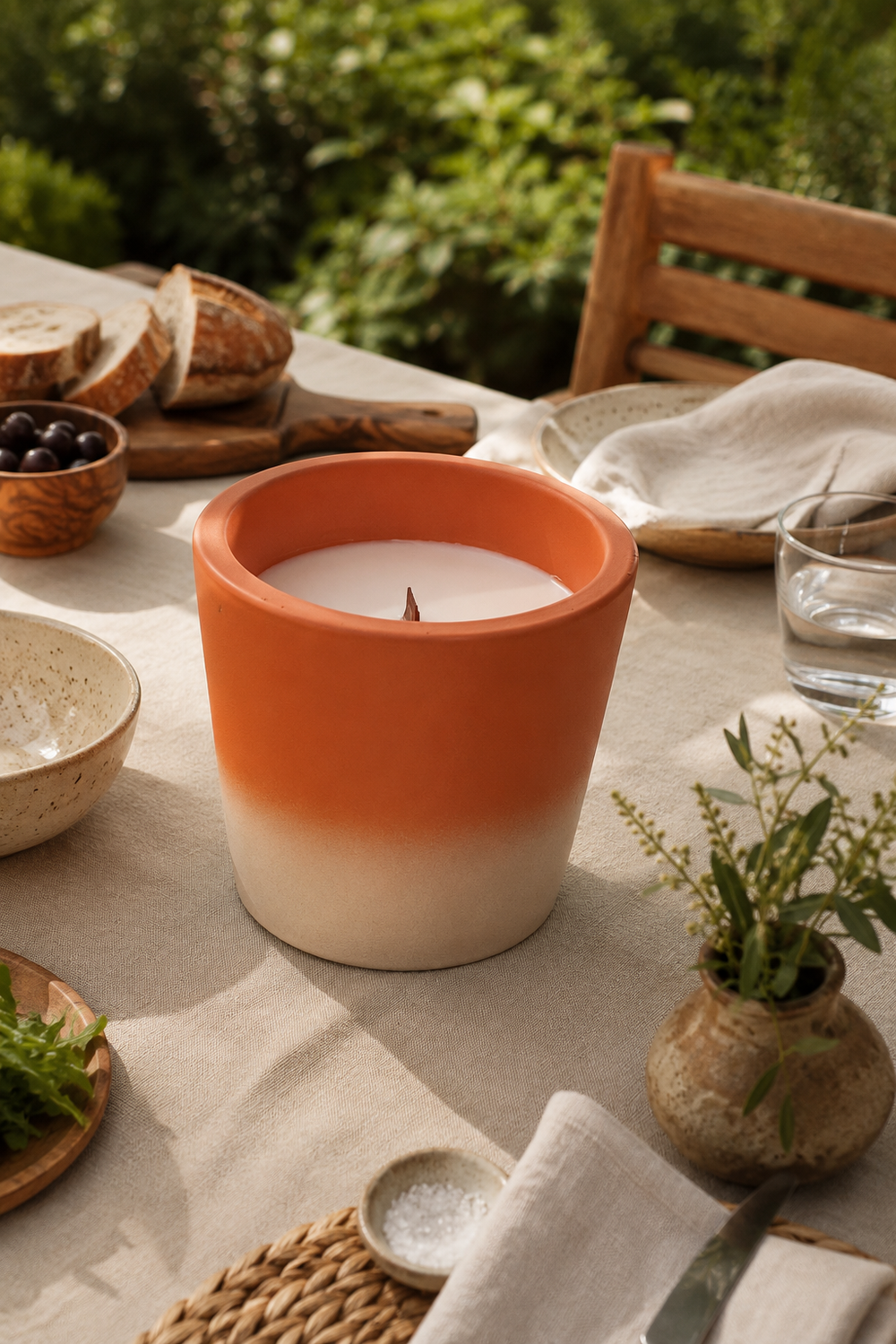 Candle in an orange and white terracotta pot on a table with bread and greens