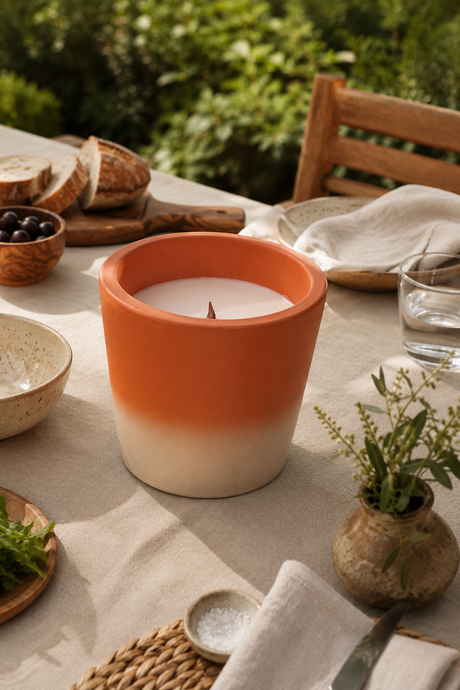 Candle in an orange and white terracotta pot on a table with bread and greens