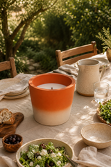 Candle in an orange and white terracotta container on a table with outdoor setting