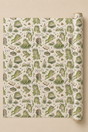 A roll of wrapping paper with a whimsical Frog with books pattern, displayed flat against a solid beige background. The pattern features various green frogs in different poses alongside books, glasses, and small plants on an off-white background.