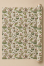 A roll of wrapping paper with a repeating pattern of Bookish Frogs at Christmas wearing Santa hats, shown partially unrolled against a solid beige background.