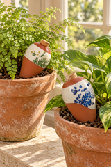 Set of two Lison terracotta watering spikes for indoor pots and planters. Features blue and green botanical designs on speckled cream bands, tapered terracotta bodies and cork stoppers. The spikes gradually release water into the soil to support regular plant care. Painted decorative finish.