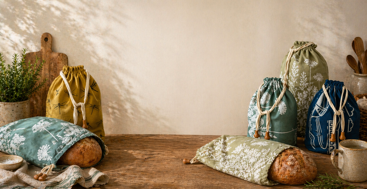 Printed linen bread bags and covered bowls arranged across a wooden kitchen worktop.