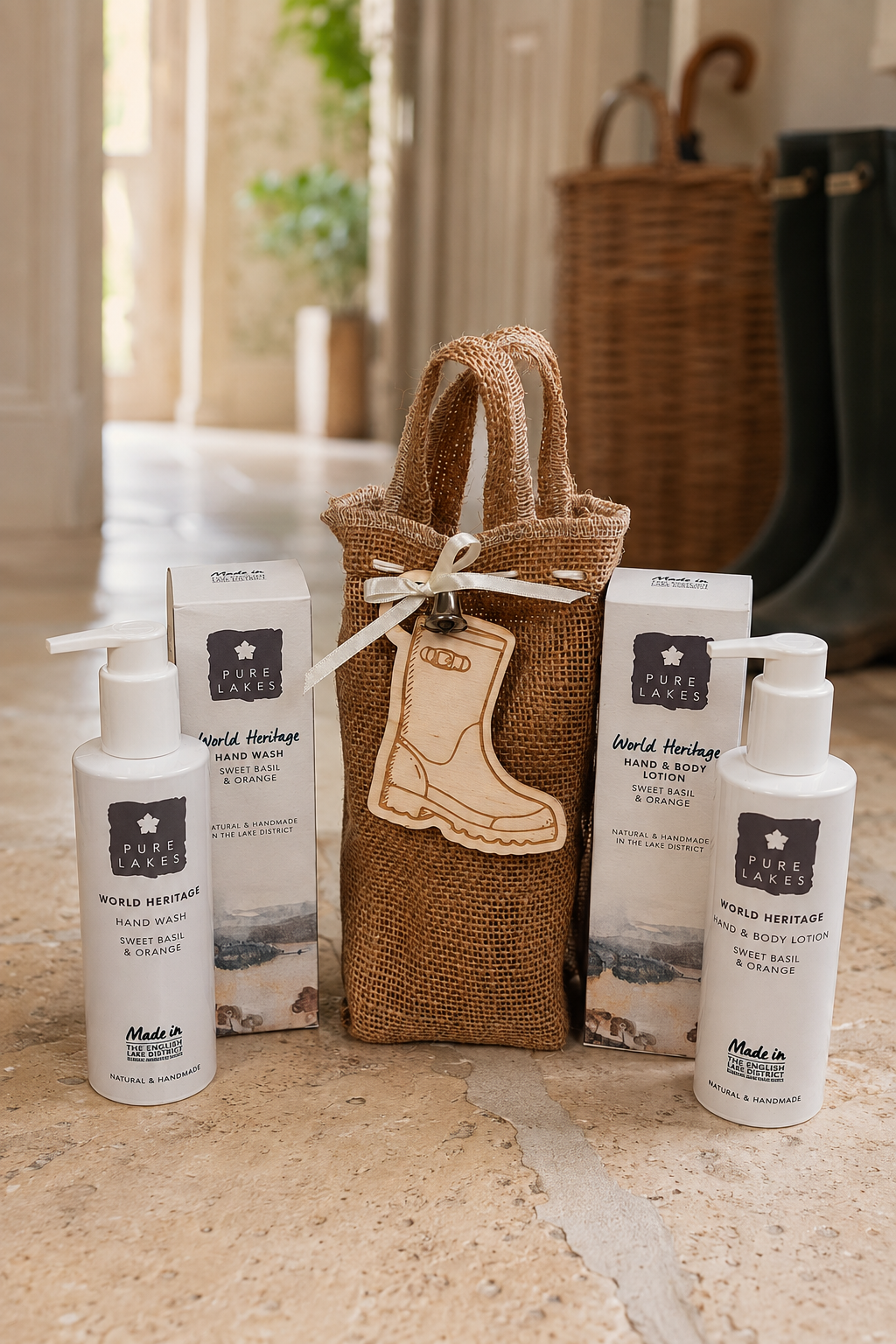 A gift set of World Heritage Cleanse products arranged on a stone surface, including two white pump bottles, two white boxes, a burlap tote bag, and a wooden boot-shaped tag, with a softly blurred indoor background.
