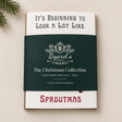 A card & envelope collection wrapped with a dark green paper band reading 'Byard's The Christmas Collection Customer Edition 2026.' The top card says 'It's Beginning to Look a Lot Like' and the bottom of the card says 'SPROUTMAS.