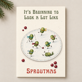 A greeting card featuring a whimsical illustration of green sprout-like characters playing hockey on a white plate, with the text 'It's Beginning to Look a Lot Like Sproutmas' on a cream background. The card is styled on a light beige surface with pine needles and red berries.