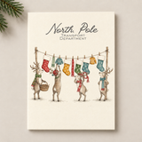 A rectangular card titled 'North Pole Transport Department' featuring an illustration of four deer hanging colourful Christmas stockings on a clothesline, shown against a light neutral background with pine branches in the corner.