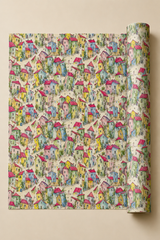 A roll of wrapping paper with a dense, colorful pattern of whimsical houses, trees, and paths on a cream background, shown partially unrolled against a solid beige backdrop.