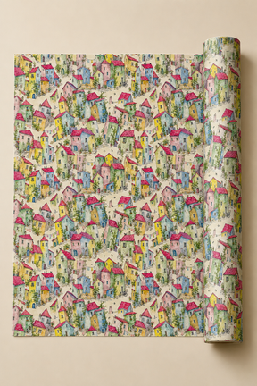 A roll of wrapping paper with a dense, colorful pattern of whimsical houses, trees, and paths on a cream background, shown partially unrolled against a solid beige backdrop.