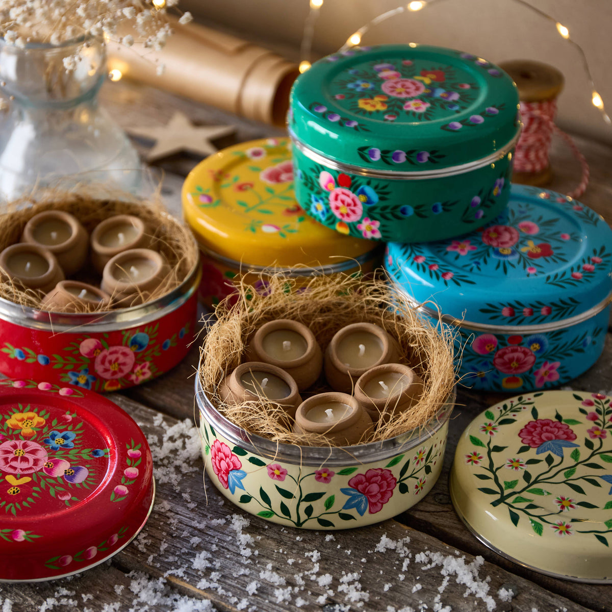 Colourful tin containers with floral designs and small candles on a wooden surface.