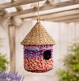 Colourful woven birdhouse hanging in a garden setting