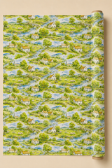 A roll of wallpaper featuring a repeating watercolor-style landscape pattern of green fields, trees, blue winding streams, and small white houses with orange roofs, shown against a warm beige background.