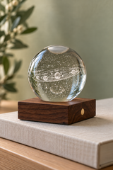 Unlit Solar System crystal lamp on a linen-covered book, showing the engraved planets and natural walnut base.