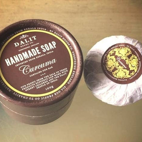 Handmade soap with a brown container and visible branding on a reflective surface.