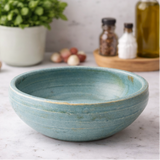 Handcrafted ceramic bowl on a wooden surface with herbs and oil.