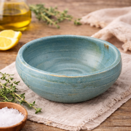 Handcrafted ceramic bowl on a wooden surface with herbs and oil.