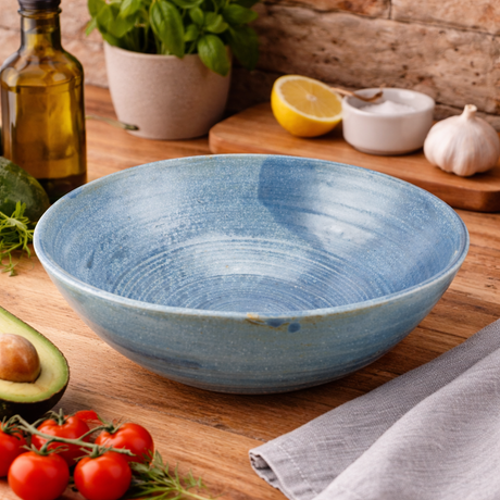 Blue ceramic bowl on a wooden table with vegetables and a plant in the background