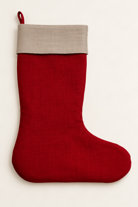 A red linen Christmas stocking made of red linen with a contrasting natural linen cuff and a red hanging loop, shown against a plain off-white background.