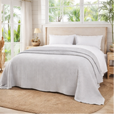 bed room with dove grey bed throw big open windows with plants outside