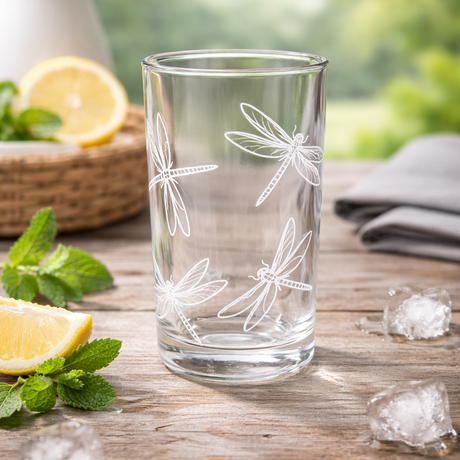 Clear glass with dragonfly designs on a wooden table with lemons and ice cubes.