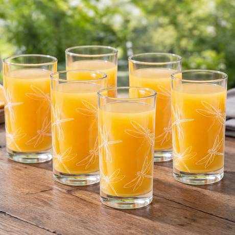 Six glasses of orange juice on a wooden table with oranges and a pitcher in the background.