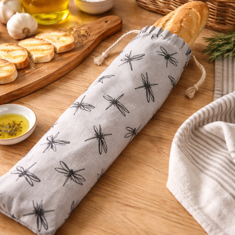 Bread wrapped in a dragonfly-patterned cloth on a wooden table with bread basket and ingredients.