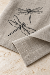 Close-up of a natural linen dragonfly napkin showing its mitred corner, double-fold hem and pale stitching.