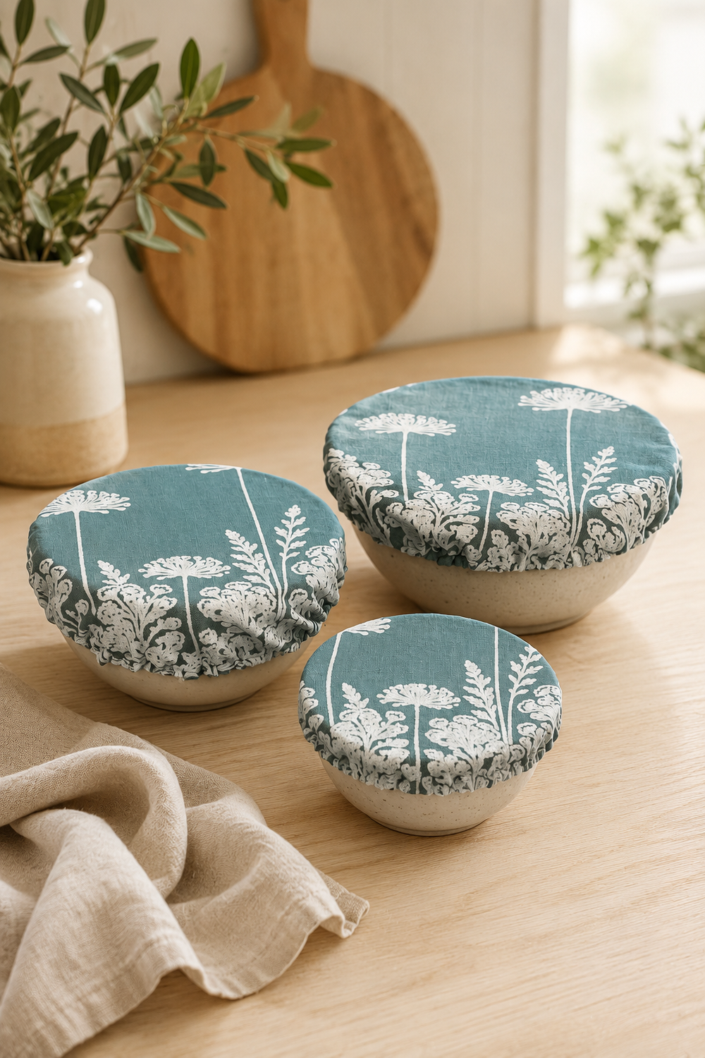 A set of three reusable Duck Egg Green Florilegium linen bowl covers, hand printed in Derbyshire with a delicate white botanical design featuring agapanthus and foxglove flowers. Lined with ProCare® FoodSAFE waterproof fabric, they are ideal for covering leftovers, salads, fruit bowls, prep bowls, cake mixtures and rising dough.